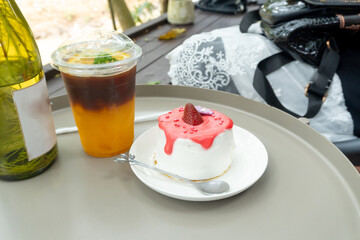 Iced lemon tea in transparent plastic glass and strawberry cake with glazed cream in mini white plate with mini silver spoon or tea spoon served to customer at a cafe