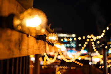 Christmas market hanging light decoration with bright light bulb and blurry, defocused, bokeh balls background. Late evening light, shallow depth of field, blue hour