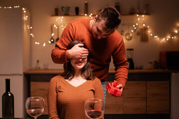 Surprise Gift for lover woman. Romantic man covering girlfriends eyes giving present box as...