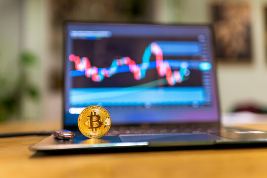 Physical bitcoin coins with wallet and financial charts displayed on laptop screen in background