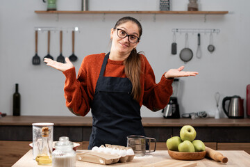 woman cooking apple pie in the kitchen, looking at camera shrugging shoulders and making I don't...