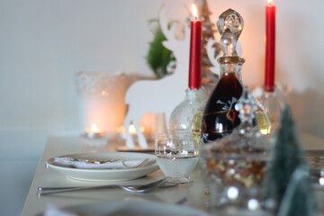 Table set for Christmas meal, with plates, wine, decorations and lit candles. Selective focus.