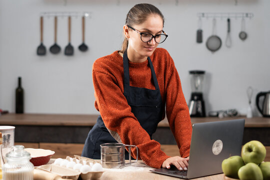 Happy pastry chef woman typing using laptop at cozy kitchen