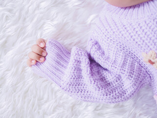 Close up of newborn baby hand is wearing a purple clothes on white bed