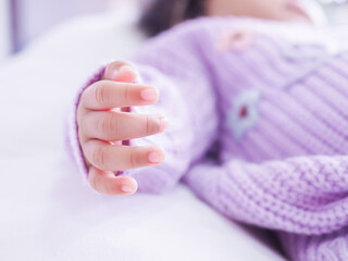 Close up of newborn baby hand is wearing a purple clothes on white bed