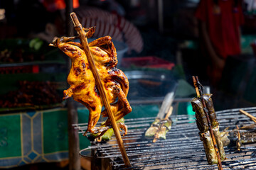 Obraz premium Grilled chicken browning on a bamboo skewer above a charcoal grill at a local street food stall in siem reap, cambodia