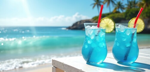 Two blue cocktails with lime slices and red straws sit on a white table. The ocean and sunny sky form a tropical beach background. Palm trees and rocks are visible on the shore.