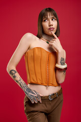 Young woman in stylish orange corset outfit poses playfully against a vibrant background