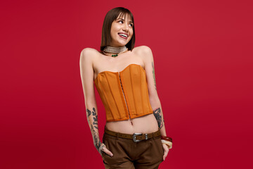 Young woman showcases vibrant style in trendy orange outfit against a bold red backdrop