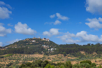 Obraz premium The medieval Ourém Castle (Castelo de Ourém) stands atop a lush green hill in the Santarém district, Portugal, overlooking a vast rural landscape.