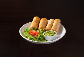 Chicken flauta platter with a fresh garden salad and guacamole in a white plate on a dark surface, appetizer, 
