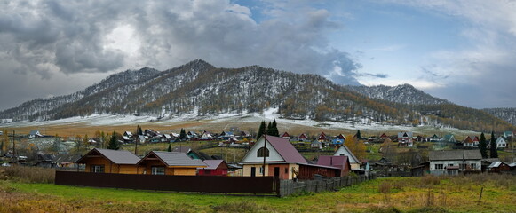 Cherga. Russia.  October 02, 2025 A picturesque view of the Altai village against the background of mountains covered with the first autumn snow, surrounded by yellow larches.