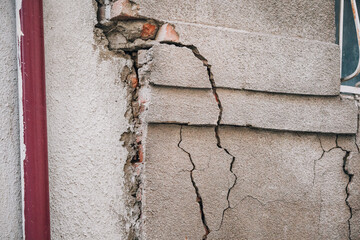Building exterior showing significant structural damage with deep cracks in the concrete facade, exposing underlying brickwork. Signs of decay