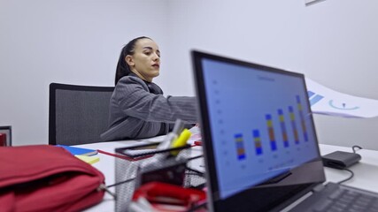 A focused professional woman diligently analyzes data and reviews important documents on her laptop in a contemporary office setting, showcasing dedication to her business tasks.