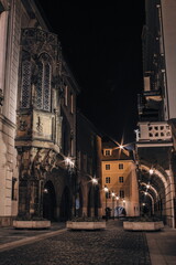 Fototapeta premium A quiet historic street in Prague illuminated by warm night lamps, showcasing ornate Gothic details, arched passageways and the timeless charm of old-town architecture after dark. 