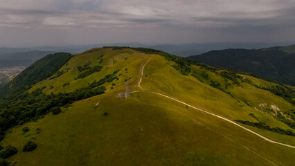 Aerial view of green hills in the Caucasus region. The landscape features winding paths and lush vegetation under a cloudy sky.