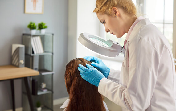 Hair examination by trichologist to check for hair loss problem, control disease and therapy. Doctor looking at head of woman with magnifying glass, lamp in hospital. Trichology, dermatology concept
