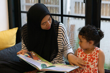 Mother reading to her child by the window seat on weekend