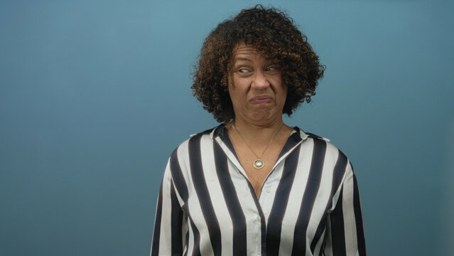 Woman wrinkles nose and frowns wearing striped shirt and gold necklace in studio; disgust aversion reaction.