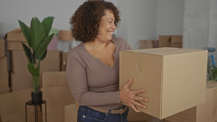 Smiling woman carrying cardboard box inside a building filled with moving cartons; fresh start optimism.