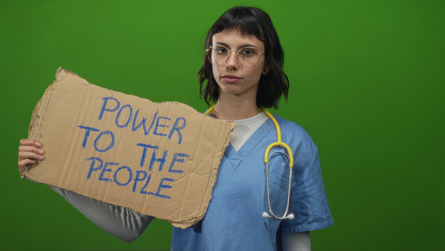 Woman wearing scrubs and holding cardboard sign reading power to the people in green studio; empowerment solidarity equality.
