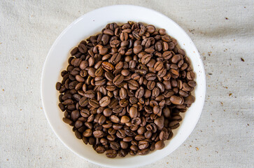 Rich Brown Roasted Coffee Beans Piled in a White Dish on a Textured Linen Background