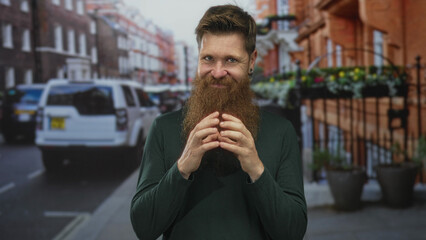 Young caucasian man with reddish beard and fingertips touching on urban street under daylight;...