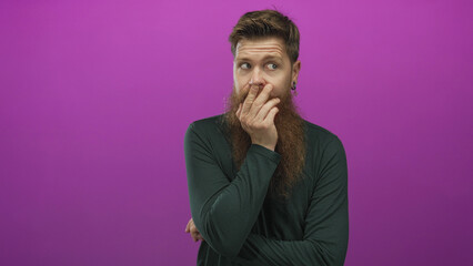 Bearded man in dark shirt presses finger to lips for silence in pink studio; surprise curiosity wonder.