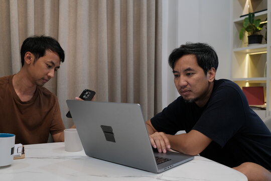Two men are sitting at a table with a laptop open in front of them
