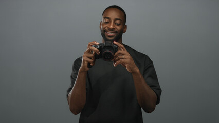 Man holding dslr camera, smiling and adjusting lens with gold chain visible in gray studio; confidence creativity inspiration.