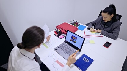 Professional business coworkers are diligently working at their office desks, reviewing charts, graphs, and digital data on a laptop. They are focused on data analysis and strategic planning. - Powered by Adobe