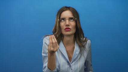 Woman with pinched fingers gesture in blue studio set wearing glasses and striped shirt; frustration.