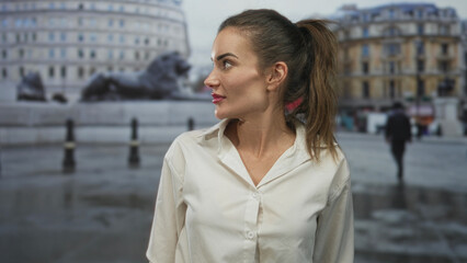 Obraz premium Woman smiling and pointing finger toward a stone lion statue on a city street with a ponytail and white shirt; excitement.