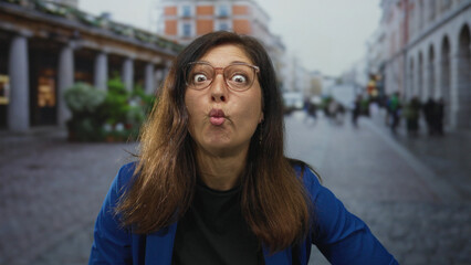 Fototapeta premium Middle aged hispanic woman pursing lips while looking upward on city street under daylight; playful amusement.