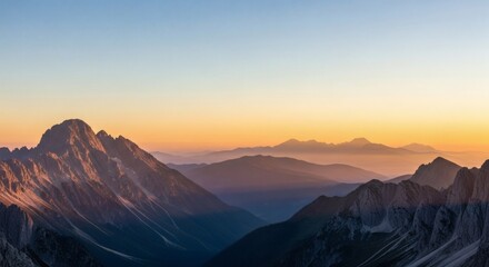 A scenic view of layered mountain ranges at sunrise, with a clear blue and orange gradient sky above.
