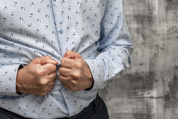 Close-up of a man's hands holding his aching stomach. A man wearing a blue long-sleeved shirt stands in a medical clinic