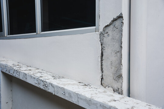 Cracked concrete wall and peeling paint below a window.