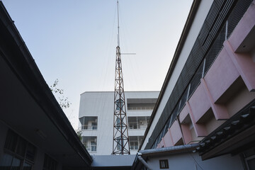 Naklejka premium Communication tower rising between buildings against clear sky.