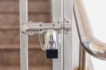 A silver padlock secures a metal gate with stairs behind.