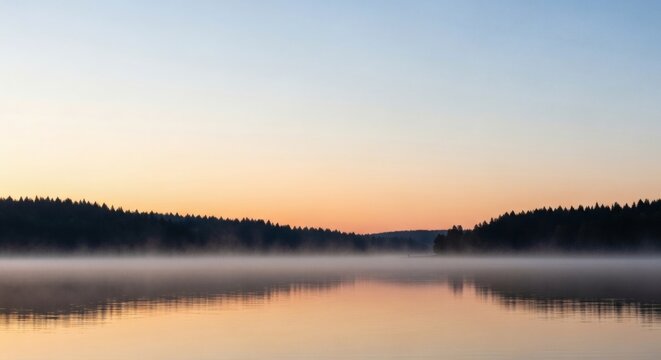 Serene morning mist rising from a calm lake reflecting the colorful sunrise sky and distant forest.