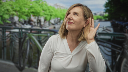 Woman wearing white blouse with hand cupped to ear beside parked bicycle on street lined with bicycle racks; curiosity.