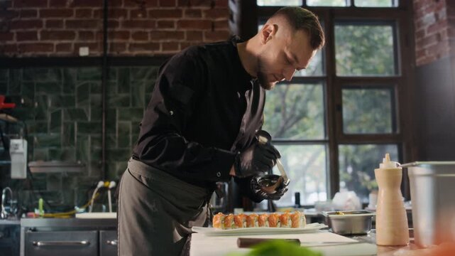 Cinematic side view shot of professional male chef putting caviar on salmon sushi roll while plating luxury dish in restaurant kitchen, copy space