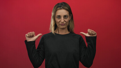 Blonde woman points both thumbs to chest in red studio with skeptical expression and raised eyebrows; skepticism.