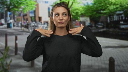 Fototapeta premium Woman shielding eyes with hand to forehead on street, palm above brow and standing with one hand on hip; fatigue urban waiting.