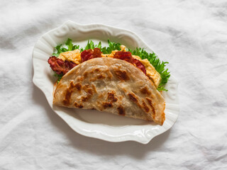 Delicious breakfast, tapas, snack - roti tortilla with omelet, bacon and green salad on a light background, top view