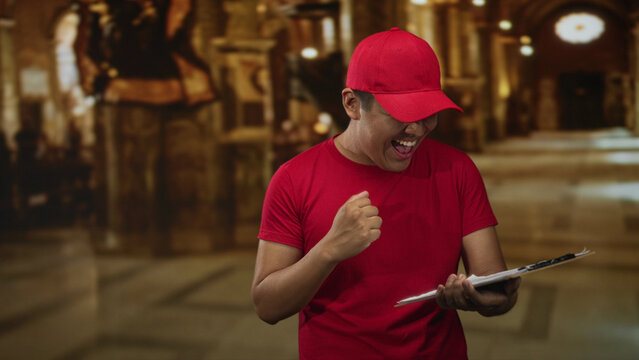 Man points finger to clipboard in building while checking document and wearing red cap and tshirt; service joy.