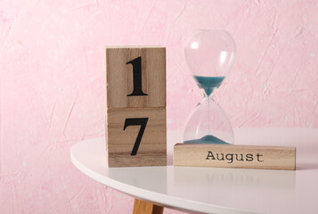 August 17 wooden block calendar and hourglass on table, pink concrete background