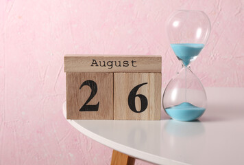 August 26 wooden block calendar and hourglass on table, pink concrete background