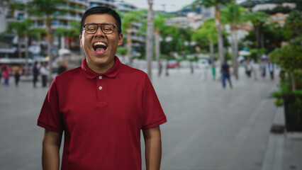 Fototapeta premium Man laughing with mouth open on a street wearing red polo and glasses, facing camera; joy confidence.