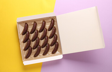 Box of chocolate candies on yellow purple background. Top view